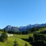 Planina s stavbami, zelenimi pobočji in skalnatim grebenom v ozadju