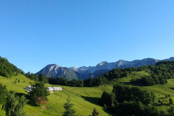 Planina s stavbami, zelenimi pobočji in skalnatim grebenom v ozadju